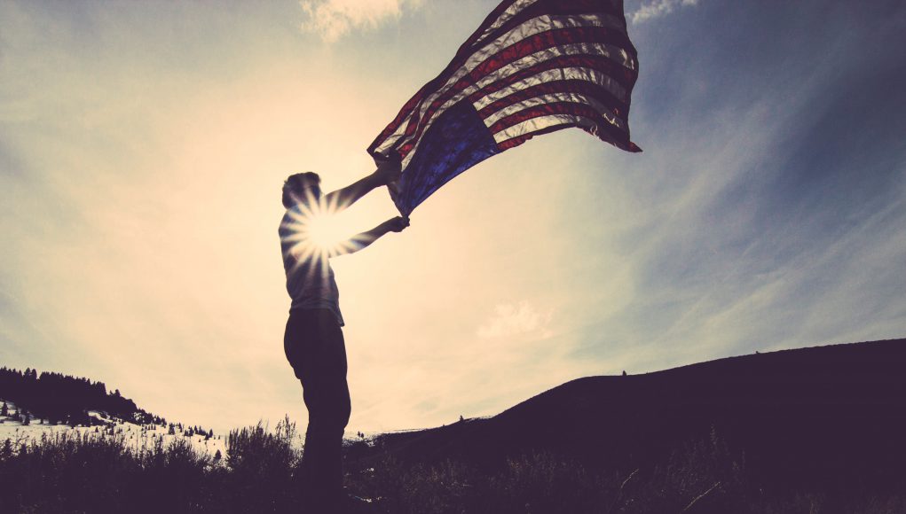 sillhouette of a person holding a flag with the sun in the background