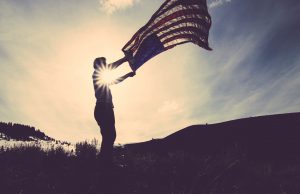 sillhouette of a person holding a flag with the sun in the background