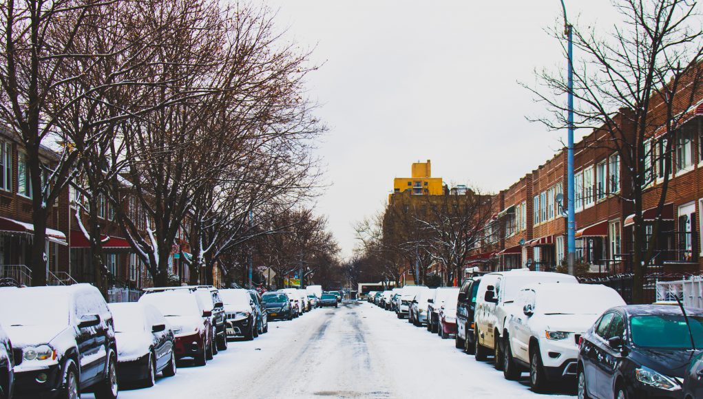 district 7: snow in the street with cars lining it and snow on top