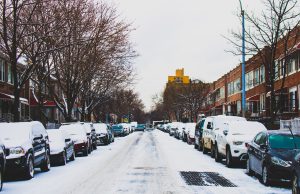 district 7: snow in the street with cars lining it and snow on top