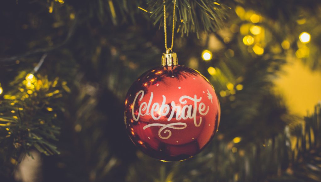 holiday: red ornament that says celebrate hanging on a tree