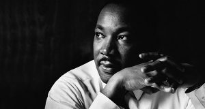 black and white image of martin luther king looking in the distance with his hands clasped