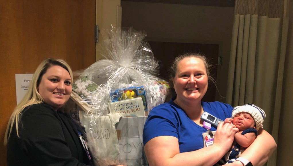 first baby: 2 nurses holding a basket full of baby items and a new born baby