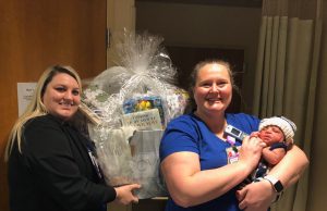 first baby: 2 nurses holding a basket full of baby items and a new born baby