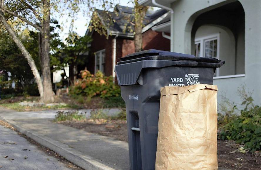 a gray trash bin with a grass clippings bag on the curb