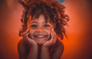 Little Ones Fundraiser: little girl smiling with a little afro and a burnt orange background