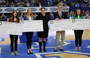 Essay Contest: four students holding checks and a woman dressed in black between them