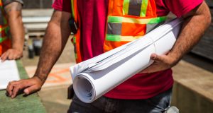 Polo Club Blvd Liberty Road: a man in a red shirt and reflective vest holding rolled up paper