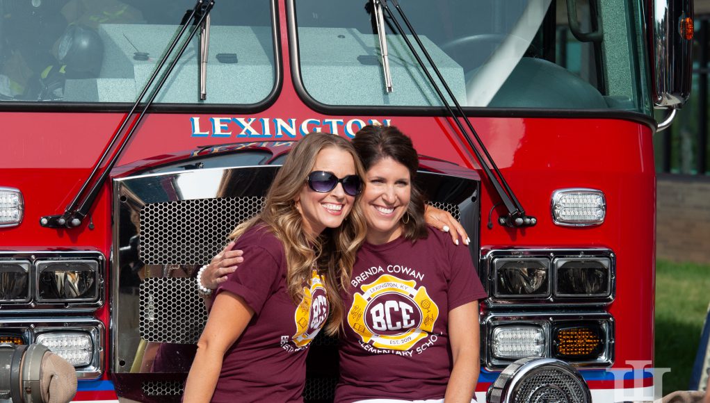 Lexington Family: two women in maroon shirts sitting in front of a fire truck smiling at a camera