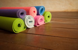 Colorful yoga mats rolled up on a wooden floor in a yoga studio.